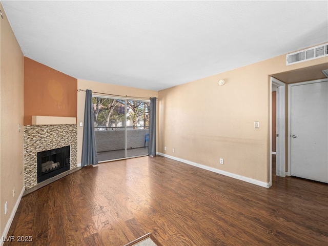 unfurnished living room with a tile fireplace, wood finished floors, visible vents, and baseboards