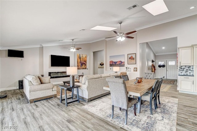 dining area featuring ceiling fan, ornamental molding, vaulted ceiling with skylight, and light hardwood / wood-style flooring