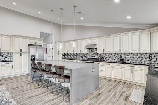 kitchen with decorative light fixtures, light wood-type flooring, dark stone counters, and appliances with stainless steel finishes