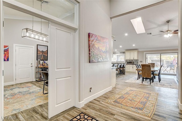 entrance foyer with crown molding, ceiling fan, a skylight, and light hardwood / wood-style flooring