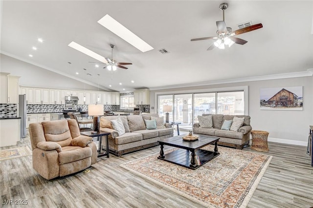 living room featuring a skylight, ornamental molding, ceiling fan, and light wood-type flooring