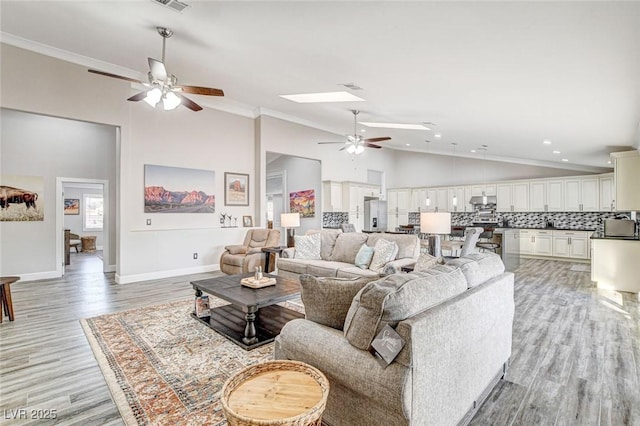 living room featuring ornamental molding, light hardwood / wood-style floors, ceiling fan, and a skylight