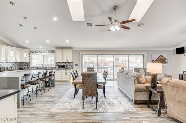 dining space with lofted ceiling, sink, crown molding, light hardwood / wood-style flooring, and ceiling fan