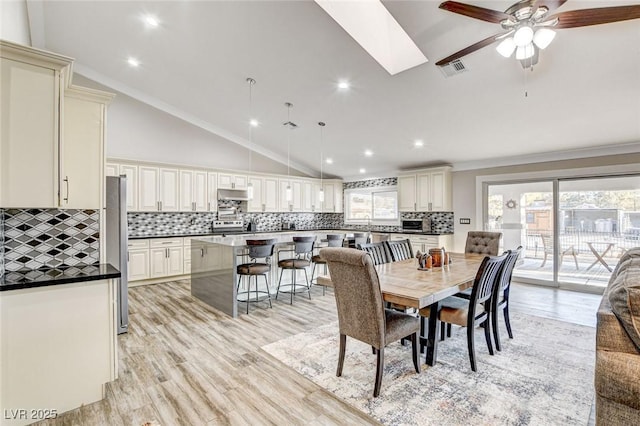 dining area with a skylight, high vaulted ceiling, light hardwood / wood-style flooring, ornamental molding, and ceiling fan