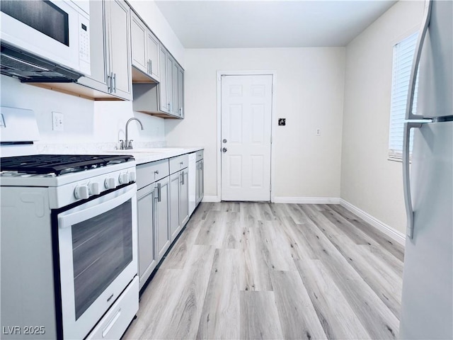 kitchen with white appliances, sink, light hardwood / wood-style flooring, and gray cabinetry