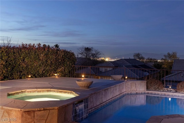 pool at dusk featuring an in ground hot tub