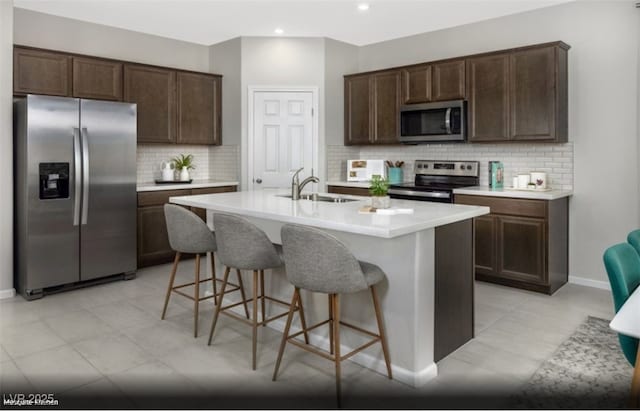 kitchen with an island with sink, stainless steel appliances, sink, and dark brown cabinetry