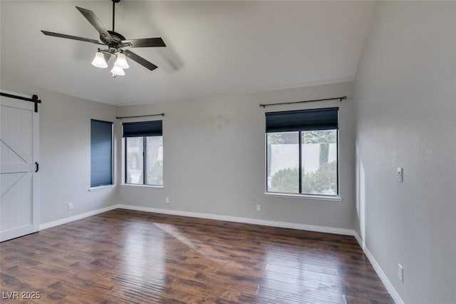 spare room featuring a barn door, dark hardwood / wood-style floors, and ceiling fan