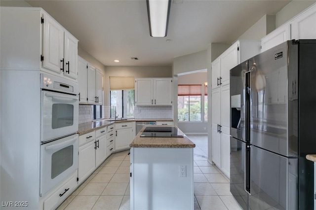 kitchen featuring a kitchen island, tasteful backsplash, white cabinets, light tile patterned floors, and stainless steel appliances