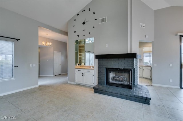 unfurnished living room featuring high vaulted ceiling, sink, light tile patterned floors, a brick fireplace, and an inviting chandelier