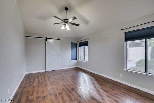 unfurnished bedroom featuring multiple windows, a barn door, dark wood-type flooring, and ceiling fan