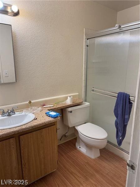 bathroom with wood-type flooring, walk in shower, vanity, and toilet