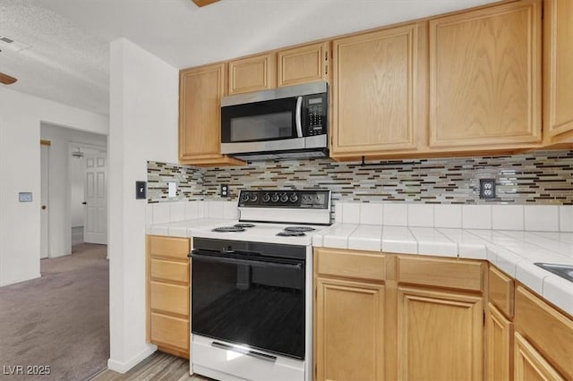 kitchen featuring white range with electric cooktop, tile counters, light carpet, and decorative backsplash