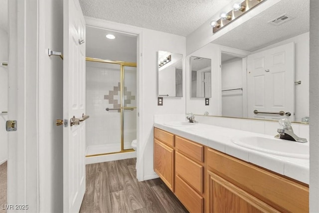 bathroom with hardwood / wood-style floors, vanity, toilet, a shower with door, and a textured ceiling