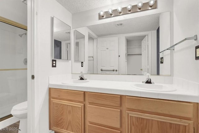 bathroom featuring vanity, toilet, a shower with shower door, and a textured ceiling