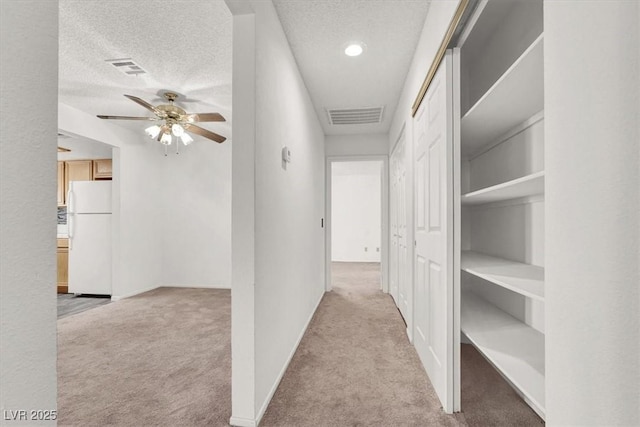 hall with light carpet and a textured ceiling