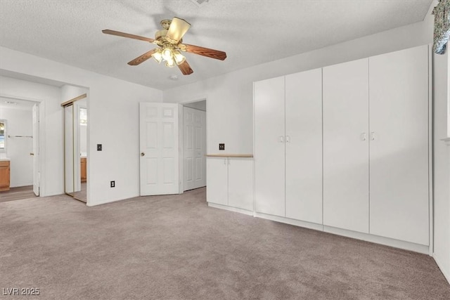 unfurnished bedroom featuring ceiling fan, ensuite bath, light carpet, and a textured ceiling