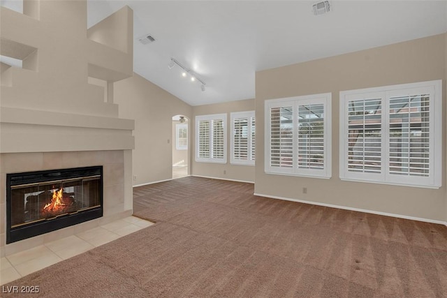 unfurnished living room with rail lighting, lofted ceiling, light carpet, and a fireplace