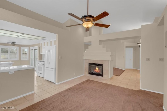 unfurnished living room with light tile patterned flooring, ceiling fan, a tiled fireplace, and vaulted ceiling