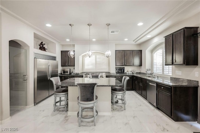 kitchen featuring dark stone counters, hanging light fixtures, a center island, stainless steel appliances, and dark brown cabinets