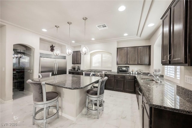 kitchen with sink, appliances with stainless steel finishes, a center island, a healthy amount of sunlight, and decorative light fixtures