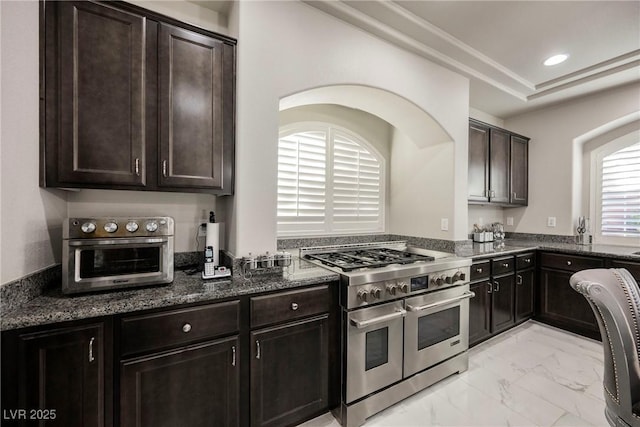 kitchen featuring range with two ovens, dark brown cabinets, and dark stone counters