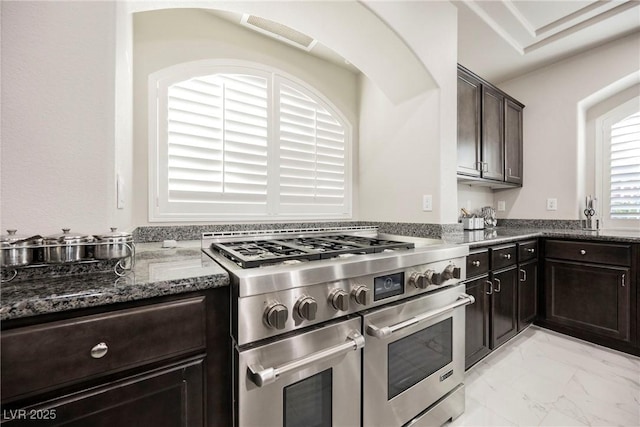 kitchen with range with two ovens, dark brown cabinetry, and dark stone counters