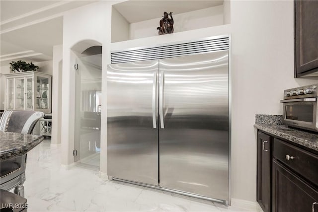 kitchen featuring stainless steel built in refrigerator, dark stone countertops, and dark brown cabinetry