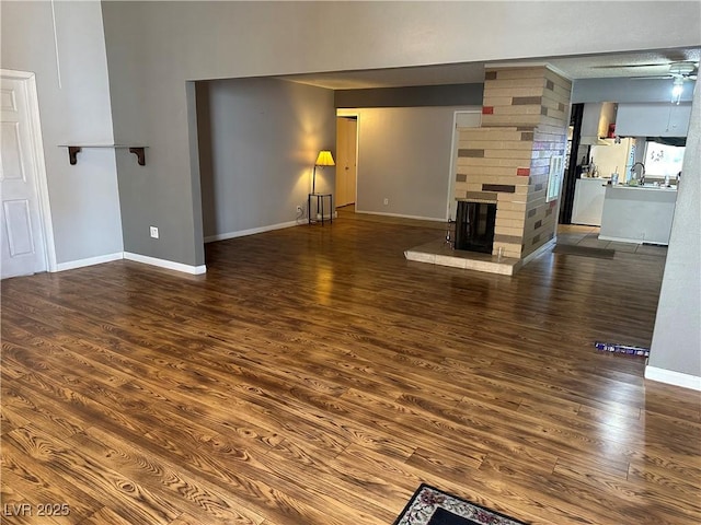 unfurnished living room with a brick fireplace, dark wood-type flooring, and sink