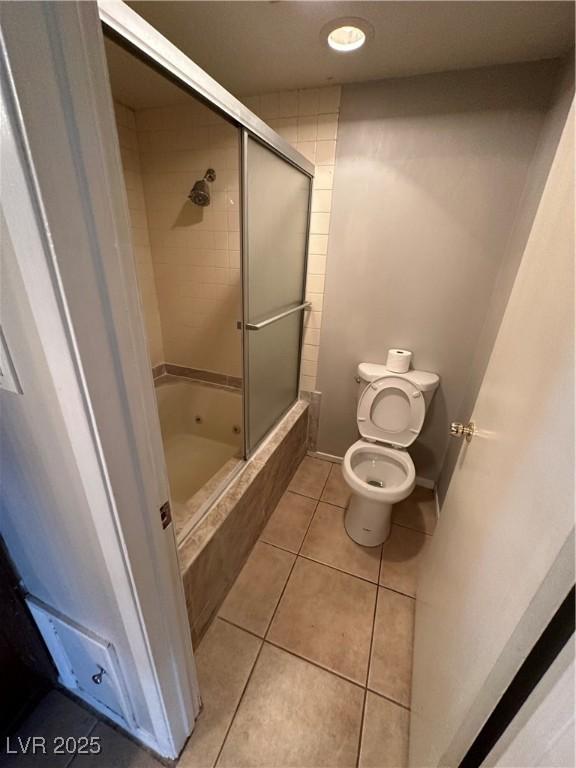 bathroom with tile patterned flooring, bath / shower combo with glass door, and toilet