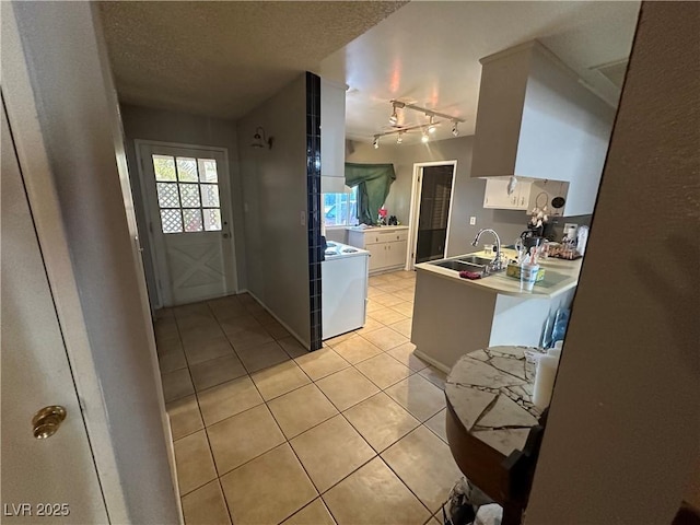 kitchen with sink, white cabinetry, a textured ceiling, light tile patterned flooring, and washer / dryer