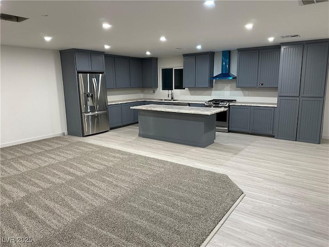 kitchen with sink, a center island, stainless steel appliances, wall chimney range hood, and light wood-type flooring