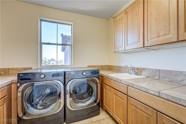 clothes washing area with cabinets, sink, washer and dryer, and light tile patterned floors