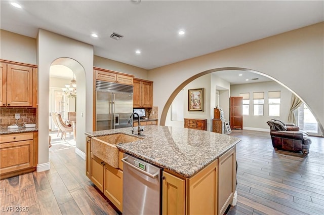 kitchen featuring stainless steel appliances, an island with sink, hardwood / wood-style flooring, and tasteful backsplash