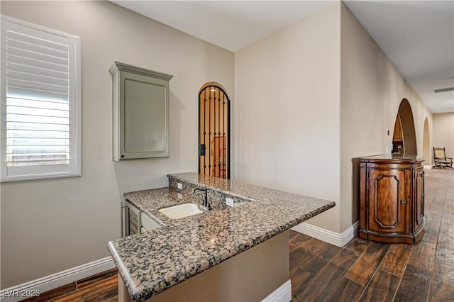 kitchen with dark wood-type flooring, kitchen peninsula, sink, and light stone countertops