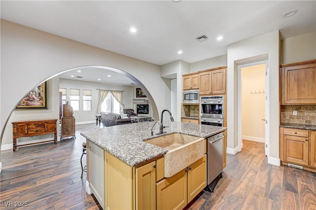 kitchen featuring sink, a center island with sink, dark hardwood / wood-style floors, stainless steel appliances, and backsplash