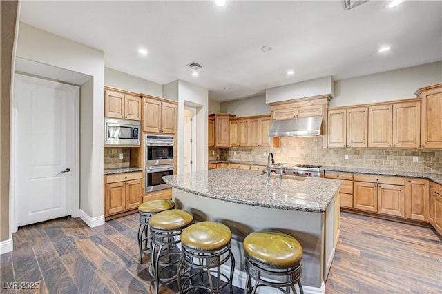 kitchen featuring an island with sink, appliances with stainless steel finishes, dark hardwood / wood-style floors, and light stone counters