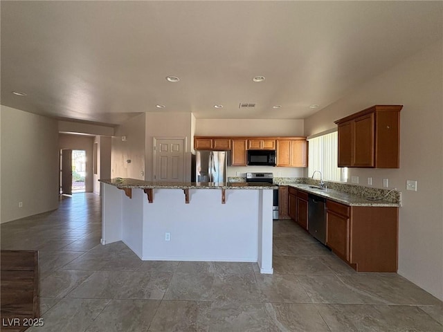 kitchen featuring a breakfast bar, sink, light stone counters, a center island, and stainless steel appliances