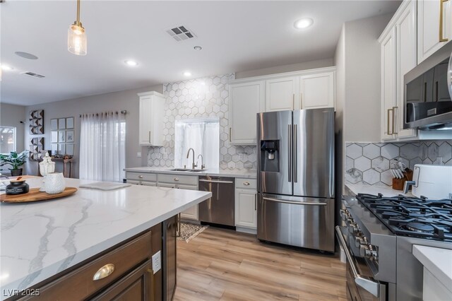 kitchen featuring sink, white cabinetry, light stone counters, decorative light fixtures, and appliances with stainless steel finishes