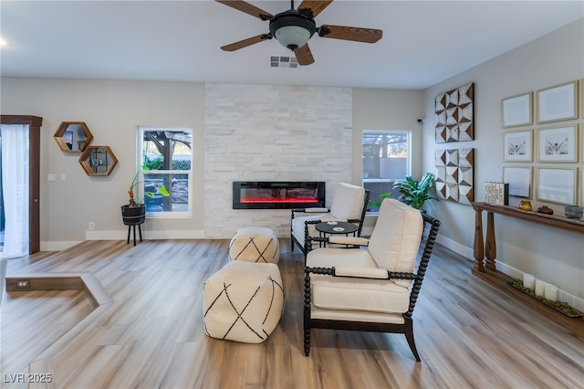 living room featuring ceiling fan, a stone fireplace, and light wood-type flooring