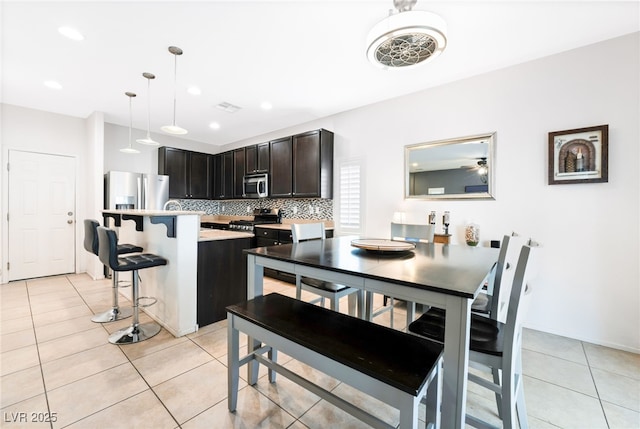 kitchen featuring backsplash, a kitchen bar, hanging light fixtures, light tile patterned floors, and stainless steel appliances