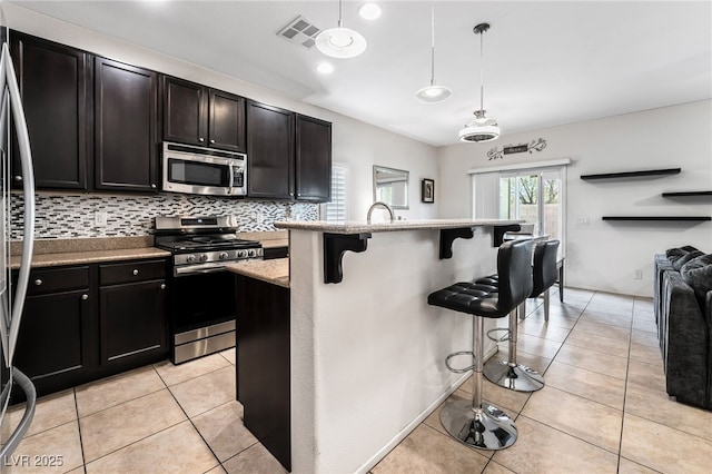 kitchen with light tile patterned flooring, a kitchen bar, appliances with stainless steel finishes, pendant lighting, and a kitchen island with sink