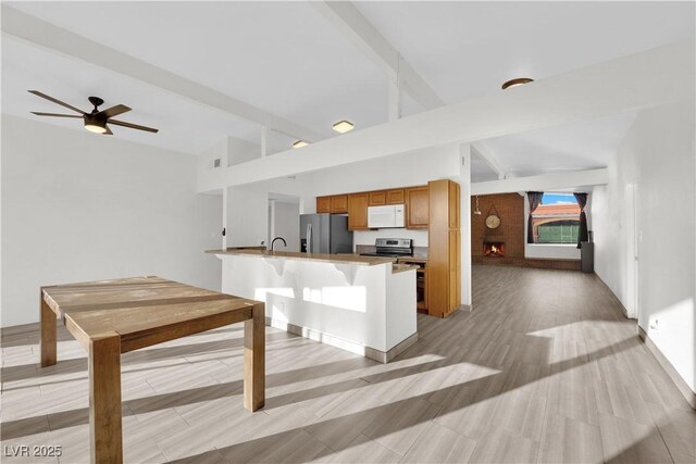 kitchen with lofted ceiling with beams, a large fireplace, a kitchen breakfast bar, ceiling fan, and stainless steel appliances