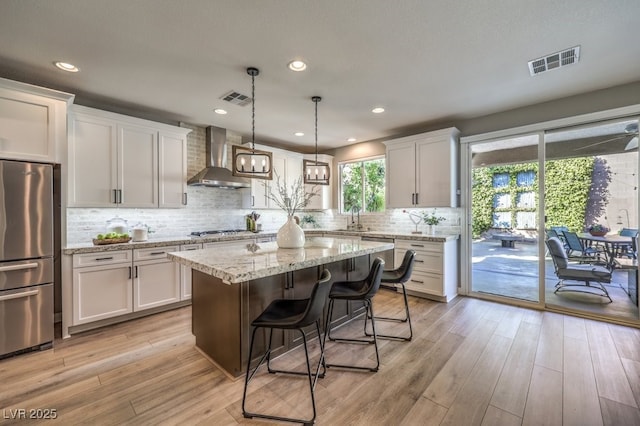 kitchen featuring white cabinetry, appliances with stainless steel finishes, a center island, and wall chimney range hood