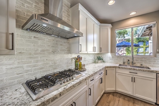 kitchen with sink, stainless steel gas cooktop, white cabinets, wall chimney exhaust hood, and light wood-type flooring