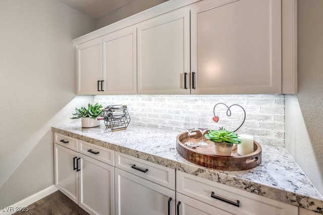 interior space with white cabinetry, dark hardwood / wood-style floors, light stone countertops, and decorative backsplash