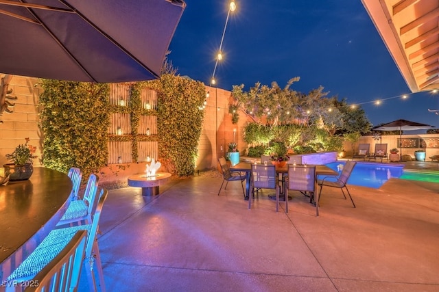 patio at night featuring a fenced in pool and a fire pit