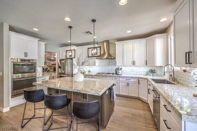 kitchen featuring wall chimney exhaust hood, sink, white cabinetry, a center island, and appliances with stainless steel finishes