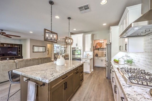 kitchen featuring white cabinetry, hanging light fixtures, a kitchen island, stainless steel appliances, and wall chimney range hood