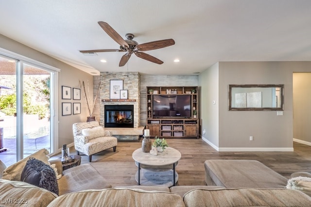 living room with ceiling fan, a stone fireplace, and light hardwood / wood-style flooring